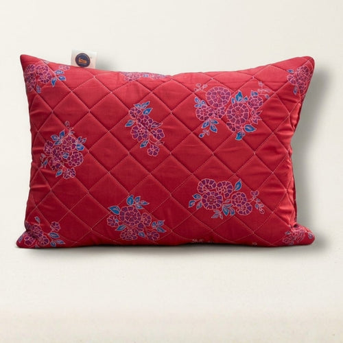 Red quilted pillow with floral patterns on a light beige background