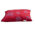Red quilted pillow with floral patterns on a white background